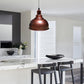 A copper-colored dome pendant light hanging over a modern kitchen island with white marble countertops and dark bar stools.