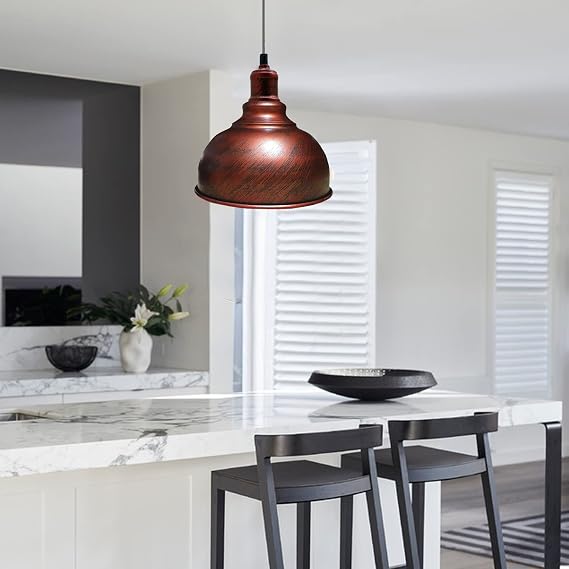 A copper-colored dome pendant light hanging over a modern kitchen island with white marble countertops and dark bar stools.
